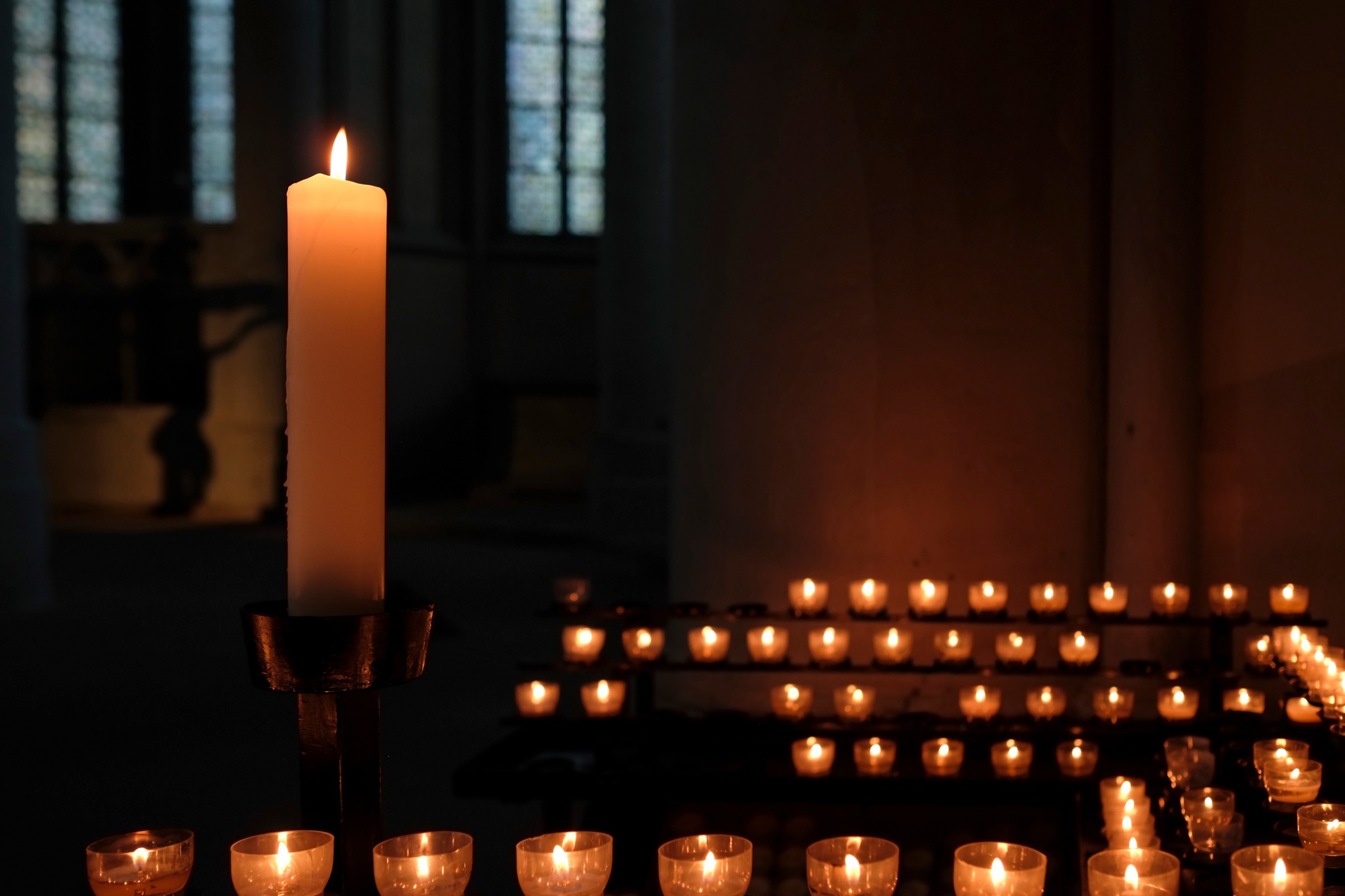 Eine große Altarkerze und viele Opferlichter in einem dunklen Kirchenraum