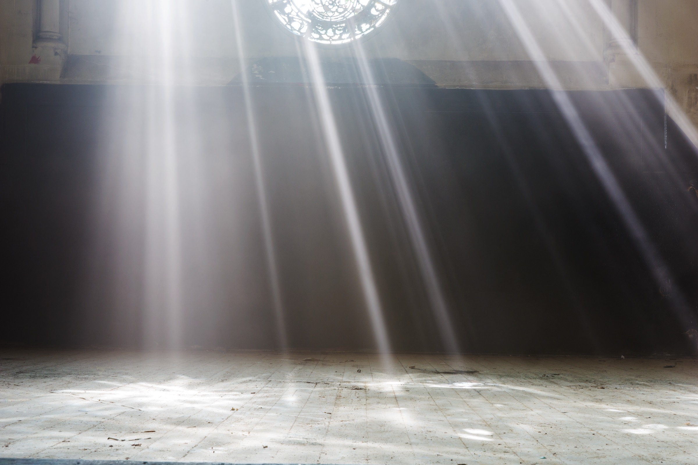 Lichtstrahlen fallen durch ein Rundfenster in einen dunklen Kirchenraum